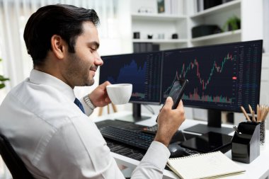 Elinde telefon dinamiğine odaklanan kahve fincanı tutan borsa yatırım ekranı veri analizini karşılaştırarak iç işlerinde yüksek kârlı finans teknolojisi pazarına yatırım yapıyor. Tahmin et..