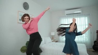 Yatak odasında Asyalı kızıyla müzik eşliğinde dans eden mutlu çekici anne. Beyaz anne dans eder ya da egzersiz yapar. Bu arada tatlı çocuk da müzik eşliğinde yatağa atlar. Aile eğlence konsepti. Pedagoji.