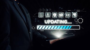 Bir iş adamı, teknoloji simgeleriyle çevrili dijital güncelleme arayüzünü gösteren bir tabletle temas kurarak, modern işyerindeki yeniliği ve ilerlemeyi sembolize ediyor. Dörtgen