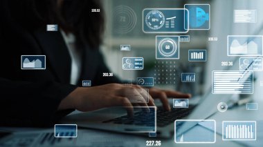 Bir iş kadını, yüksek teknolojili bir ofis ortamında, anahtar performans ölçümleri ve eğilimleri gösteren dijital grafikler ve grafiklerle birlikte, bilgisayarındaki verileri analiz ediyor. Xenic