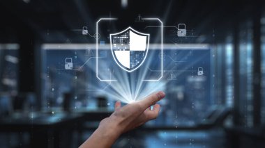 Çağdaş bir ofis alanındaki güvenliği sembolize eden dijital bir kalkana uzanan bir el, veri koruması ve siber güvenlik stratejilerinin önemini vurguluyor. Auvana
