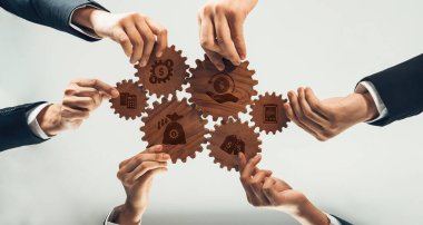 Bu resim, maliyet azaltma ve verimlilik artışını temsil eden vitesleri birbirine bağlayan ellerle takım çalışmasını vurgulayan iş stratejisindeki işbirlikçi bir çabayı betimlemektedir. Dostluk