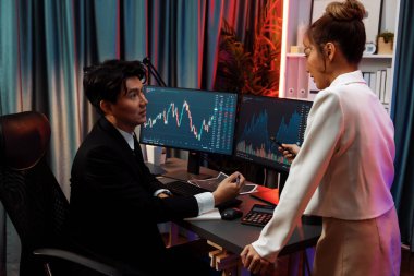 Asyalı iş kadını partneriyle dinamik borsa grafiğini tartışmak için ayakta duruyor ve geceleri neon ışığı altında çevrimiçi kar değeri web sitesi uygulamasında döviz kuruna dikkat çekiyor. İnfobahn.