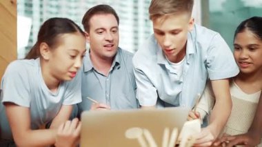 Beyaz bir öğretmen, genç bir öğrenciye nasihat verirken, bir çocuk da ders veriyor. Profesyonel eğitmen, masada dizüstü bilgisayarı ve kağıdı olan çok kültürlü çocuklarla çevrili yorumlar yazar. Öğretim