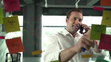 Profesyonel işadamı renkli yapışkan notlara yazılmış pazarlama stratejisi fikrine bakarken müşterilerine telefon ediyor. Proje yöneticisi duvardaki telefon analiz verileriyle konuşuyor. Yönlendirici.