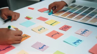 Renkli notlar ve kumaşlarla beyin fırtınası yapan dinamik bir ofis sahnesi projeler için işbirliği ve yaratıcı planlamayı vurguluyor. SACTR