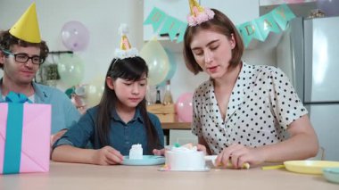 Kafkasyalı anne doğum günü pastasını kesiyor ve babaya verirken tatlıyı ayırıyor. Mutlu aile, kızının doğum gününde masada otururken parti şapkası takar. Özel durum konsepti. Pedagoji.