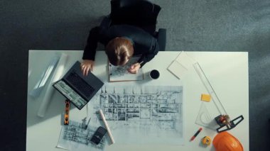 Dizüstü bilgisayarda çalışırken mimari çizimlerin hava görüntüsü. Kafkasyalı mühendisin bina modelini tasarlayıp, ekipman ve güvenlik kaskıyla birlikte tasarladığına dair tepeden aşağı bir bakış açısı. Hizalama.