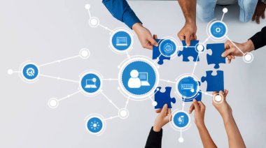 Çeşitli eller, teknoloji ve iletişimi temsil eden dijital simgelerin yanı sıra bir iş ortamında takım çalışmasını ve işbirliğini simgeleyen mavi yapboz parçalarını bir araya getirirler. Dostluk