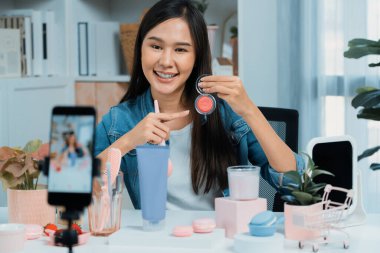 Genç, güzel Asyalı makyaj fırçası yanak testi koleksiyonunu pastel renkle inceliyor. Sosyal medyada akıllı telefonu tanıtmak için pembe ile ışıltılı bir ruh hali sergiliyor. Taktik.