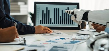 Modern bir iş toplantısı, dijital ekrandaki grafiklerle etkileşen, teknolojiyi ve işbirliğini vurgulayan bir robot kolla veri analiz eden bir ekibi gösteriyor. Noogenesis