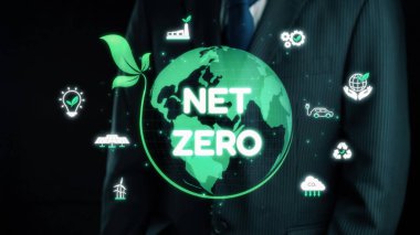 Bir iş adamı net sıfırı temsil eden parlayan yeşil kürenin yanında duruyor ve şirket sorumluluğunda sürdürülebilirliğin ve çevre dostu uygulamaların önemini vurguluyor. Dörtgen