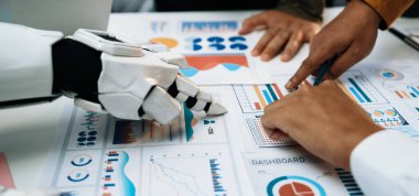 Bir robot el ve insan eli stratejik bir iş toplantısı sırasında çeşitli veri tabloları ve gösterge tablolarının ortak analizini yapar. Noogenesis