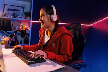 İnternet üzerinden kulaklık takıp gülümseyen Asyalı güzel kız flamasının sunucu kanalı izleyicilerle internet üzerinden konuşma yapıyor. Esport yetenekli takım oyuncuları neon mavi odada. Taktik.