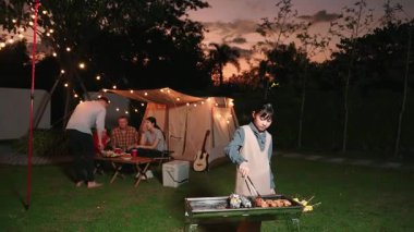 Aile hep birlikte bahçede kamp kurar, tatlı kız ızgara yapar aile ferdi için. Doğayla iç içe olmak ve ebeveynlerle ya da son sınıfların çapraz kuşaklarıyla zaman geçirmek için açık hava kamp aktiviteleri. Uyumsuzluk.