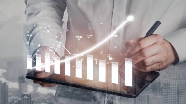 Bir iş adamı dijital tablet üzerindeki mali verileri analiz ederek, büyümeyi ve stratejiyi sembolize eden kentsel bir arkaplan karşısında büyüyen bir tablo sergiliyor. Copula