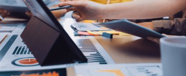 Bir iş toplantısı sırasında çeşitli profesyonellerden oluşan bir grup, dijital tabletle ilgili raporları analiz ederek işbirliği yapıyor. Renkli yapışkan notlar ve grafikler çalışma alanını genişletiyor. SACTR