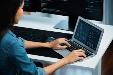 IT geliştiricisinde gülümseyen genç Asyalı dizüstü bilgisayarında kodlama programı verileriyle kotlu tişört giyerek çevrimiçi bilgi yazıyor. Güvenlik analizi iki ekran ile çevrili. Taktik.