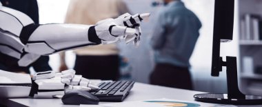 Gelecekçi bir robotik el bir bilgisayar klavyesine bağlanır, profesyoneller arka planda işbirliği yaparken, teknolojinin iş akışlarına entegrasyonunu gösterir. Noogenesis