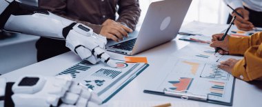 Dinamik bir iş toplantısı, insan ve robot arasındaki sinerjiyi bir dizüstü bilgisayardaki grafikleri ve verileri analiz ederken, modern işyeri yeniliklerini vurguluyor.