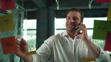 Profesyonel işadamı renkli yapışkan notlara yazılmış pazarlama stratejisi fikrine bakarken müşterilerine telefon ediyor. Proje yöneticisi duvardaki telefon analiz verileriyle konuşuyor. Yönlendirici.