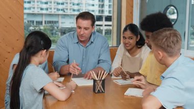 Çok kültürlü çocuklar resim çizerken ya da masa başında kalemle kağıt üzerinde not alırken zeki öğretmen konuşuyor ve işi anlatıyor. Otururken çeşitli öğrenci çizimleri ya da paylaşım fikirleriniz kutlu olsun. Öğretim