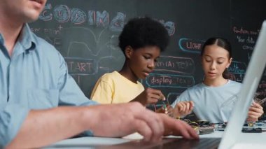 Genç öğrenci BTMM sınıfında öğretmenlik mühendisliği kodları yazarken denetleyiciyi tamir ediyor. Akıllı kız elektronik alet ve karatahta kullanırken eğitmen el bilgisayarı. Öğretim