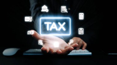 Mali sembollerle çevrili, karanlık bir ortamda parlayan bir vergi simgesini gösteren bir el uzanıyor. Finansal hizmetleri, danışmanlık ve teknolojiyi temsil ediyor. Dörtgen