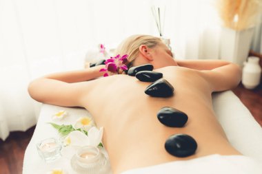 Lüks tatil köyündeki kaplıcalarda sıcak taş masajı. Gün ışığı sükunet ortamında, mutlu kadın müşteri bazalt taş masajından zevk alıyor. Rahatlatıcı bir sıcaklıkla vücudun üzerinde süzülüyor. Sessiz.