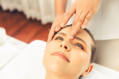 Yakın plan kadın stres önleyici kafa masajı yapmaktan ve lüks tatil beldesi veya otel spa salonundaki modern ışık ortamında yüz güzelliği eğlencelerini şımartmaktan zevk alıyor. Sessiz.