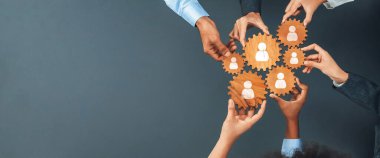 Bu resim, insan simgeleriyle ahşap vitesleri tutan, profesyonel bir çevrede işbirliğini ve ağ oluşturmayı sembolize eden elleri gösteriyor. Takım oluşturma kavramları için ideal. Dostluk