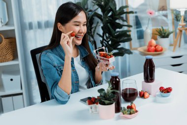 Gülümseyen, güzel Asyalı genç, lezzetli karışık çilek ve kiraz suyu detoksu içeceklerini inceleyen, sosyal medyada özel promosyon satışı için sağlıklı ürünler sergileyen. Taktik.