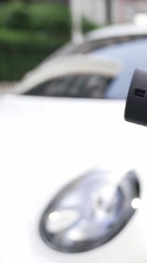 İlerici iş kadını şehir merkezinde dolaşmadan önce şarj cihazından elektrikli arabasına şarj prizi takıyor. Çevre dostu şarj edilebilir araba, sürdürülebilir ve temiz enerjiyle çalışıyor..