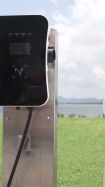 İlerici elektrikli araç konsepti, EV araba şarj istasyonu ile birlikte. Yeşil arazinin doğal arka planında göl ve yeşil tepe yenilenebilir enerjili eko-otomobilden temiz çevre için.