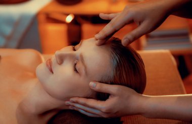 Kafkasyalı kadın stres önleyici kafa masajını yapmaktan ve lüks otel veya otelde sıcak mum ışığında yüz güzelliğini şımartmaktan zevk alıyor. Sessiz.