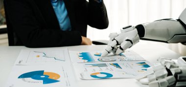 Bir insan ve bir robot modern bir çalışma alanında işbirliği yapıyor. Robot veri tablolarına işaret ederken, insan kahveden zevk alıyor. Analizde gelecekteki işbirliğini simgeliyor. Noogenesis