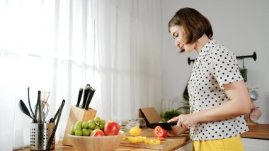 Enerjik anne, mutfak malzemeleri ile çevrili sebzeleri doğrarken modern mutfakta kahvaltı için salata yapıyor. Akıllı kadın temizlikçi yemek pişirir ve yemek hazırlar. Sağlıklı bir yaşam tarzı. Pedagoji.