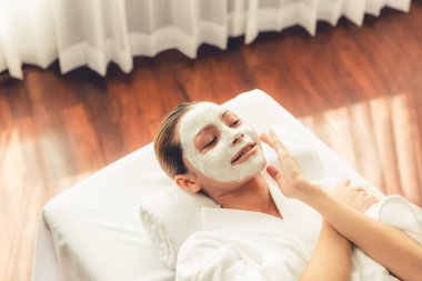 Kaplıca salonunun sakin atmosferi, masaj masasında uzanan güzel kadın, gülümseyen ve gençleşen yüz kremi spa masajı. Yüz masajı ve güzellik konsepti. Sessiz.