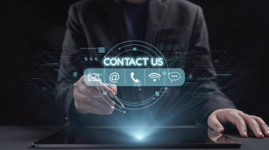 Bir işadamı, müşteri desteği için modern iletişim yöntemlerini sembolize eden bir tablet üzerinde çeşitli iletişim seçeneklerini gösteren dijital bir arayüzle etkileşime girer. Dörtgen
