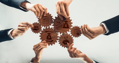 Çeşitli ellerin vergi simgeleriyle ahşap dişlileri tutması, iş dünyasındaki işbirliğini ve stratejik büyümeyi sembolize eden, finans alanındaki takım çalışmasının görsel bir temsili. Dostluk