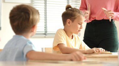 Beyaz bir çocuk ödevlerini yaparken ve açıklama dinlerken güzel bir öğretmen sınavı açıklıyor. Sınıfta not alırken ya da kağıda cevap yazarken öğretmenine bakan sevimli bir çocuk. Pedagoji.