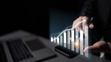 Bir işadamı, modern bir çalışma ortamında etkili bir karar verme mekanizmasında grafik verileri gösteren bir akıllı telefon kullanarak finansal büyüme eğilimlerini analiz eder. Etki