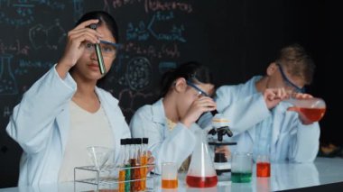 Öğrenci tahtada teoriyle deney yaparken güzel bir kız mikroskop altında araştırma yapıyor. Genç bilim adamı renkli çözeltiyi deneysel ekipmanlarla inceledi. Öğretim