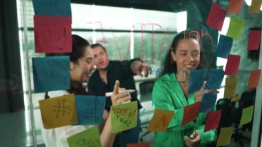 Profesyonel iş adamları, cam duvarda yaratıcı fikirleri paylaşmak için yapışkan notlar kullanarak pazarlama fikrini araştırıyor. Bir grup farklı iş adamları strateji hakkında tartışıyorlar. - Yakın çekim. Yönlendirici.