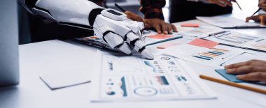 Bir robot kol modern bir ofis masasında insan işçilerle işbirliği yapar, veri analizi, grafik sunumları ve stratejik planlama faaliyetleri ile ilgilenir.