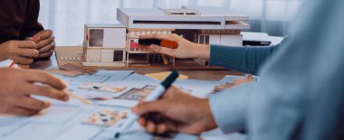 Bir ofis ortamındaki yaratıcılığı, takım çalışmasını ve tasarım sürecini vurgulayan, eskizler ve detaylı bir model üzerinde çalışan mimarların yer aldığı canlı bir işbirliği sahnesi. SACTR