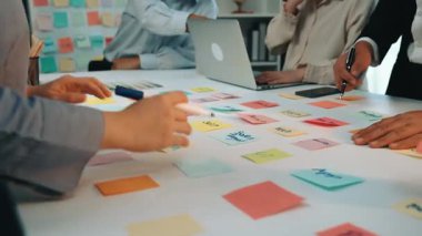 Uyumlu bir ekip, ortak çalışma alanı etrafında üretken tartışmalar yaparken renkli yapışkan notlar kullanarak fikirleri iletmek için modern bir ofiste işbirliği yapıyor. SACTR