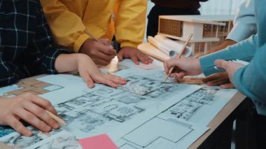 Yaratıcı profesyonellerin mimari planlar ve malzemelerle meşgul olduğu, yenilik ve takım çalışmasını teşvik ettiği, işbirlikçi bir tasarım oturumunu canlı bir şekilde yakalayan bir sahne. SACTR