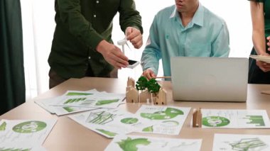 Yel değirmeni modeline ve ev şeklindeki bloğa danışmanlık yapan işadamları, Dünya Yöneticisi 'nin dizüstü bilgisayar üzerinde çalışmasını kurtarmak için yeşil enerji kullanımına referans olarak başvuruyorlar. Tanımlama.