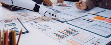 Çeşitli profesyonel bir ekip, veri analizi ve iş stratejisi gelişiminde verimliliği artırmak için robotik bir kol kullanarak ofis ortamında işbirliği yapmaktadır.